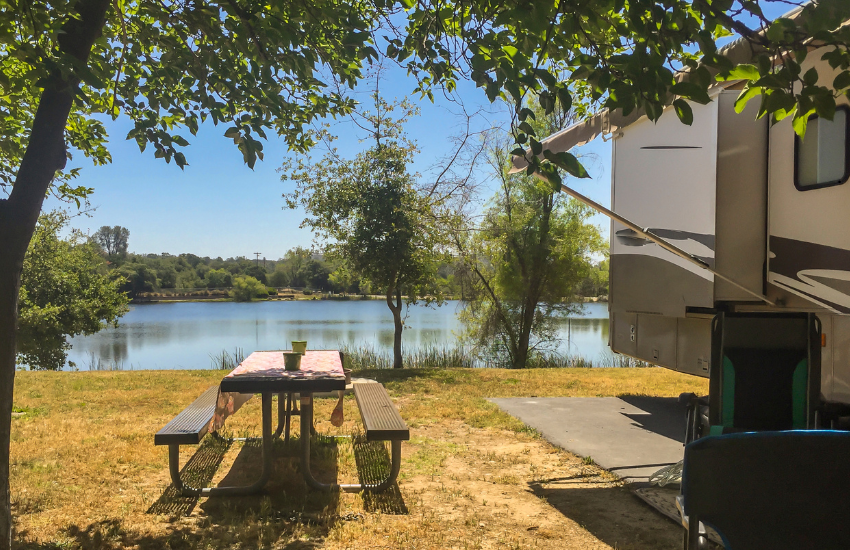 A picnic bench next to an RV by a lake.