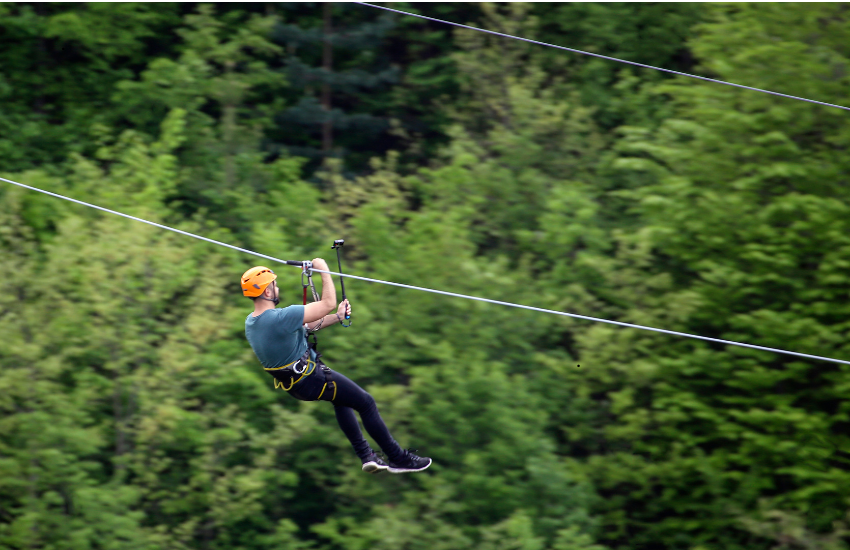 man on a zip line against backdrop of green trees