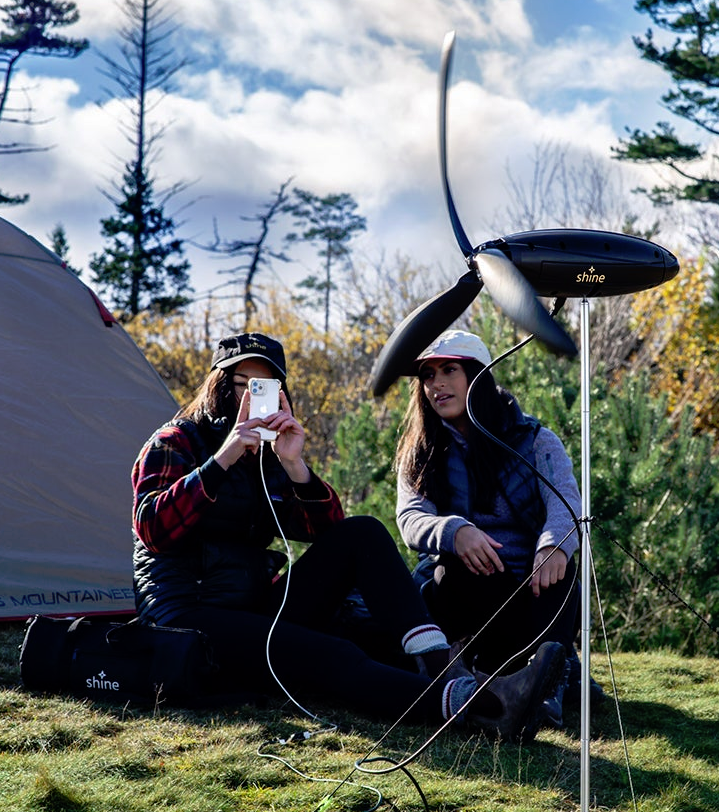 To women sat outside a tent with a portable wind charger.