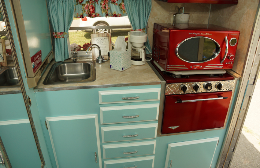 Blue cabinets and a red oven and microwavew in an old travel trailer.