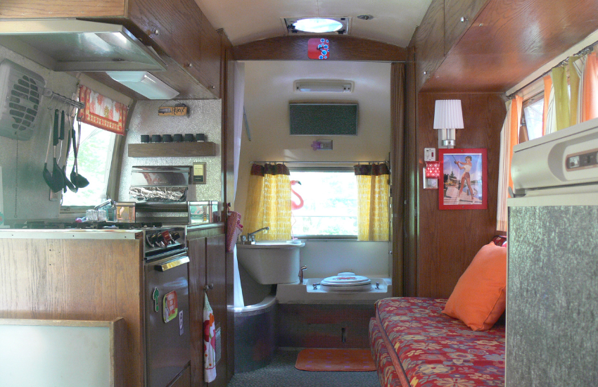 An old camper interior with floral seats and bathroom at the rear.