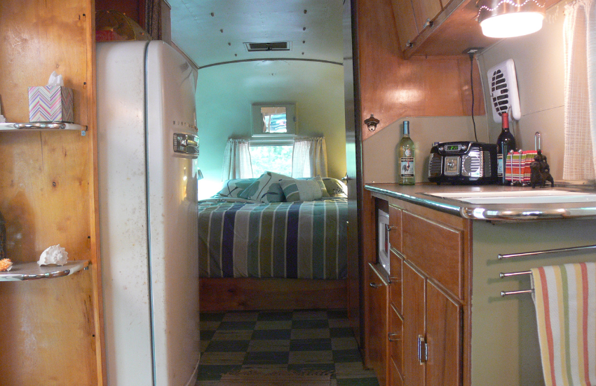An old travel trailer interior with stripey fabric bed at the rear.