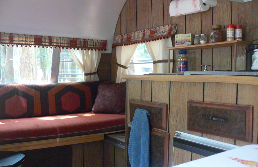 An older RV interior with wooden paneling and a red bench seat.