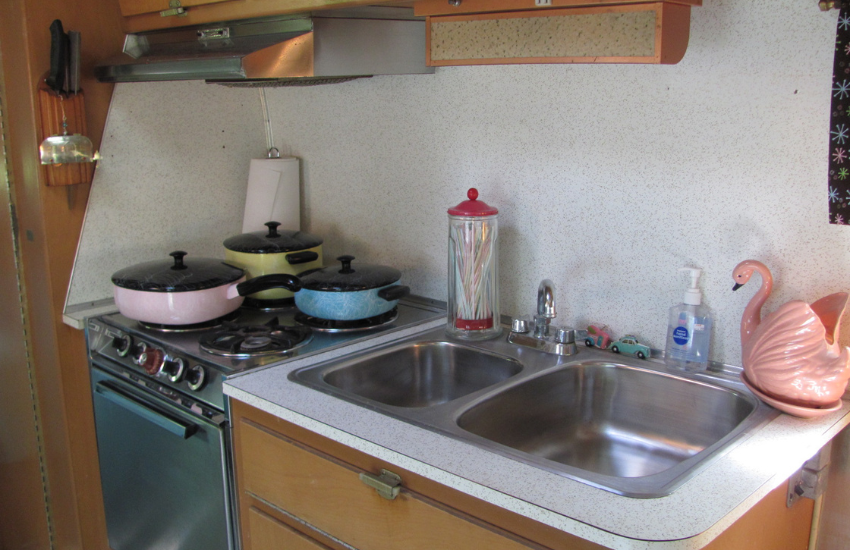 A retro camper trailer kitchen with multicolored pots on the cooker.