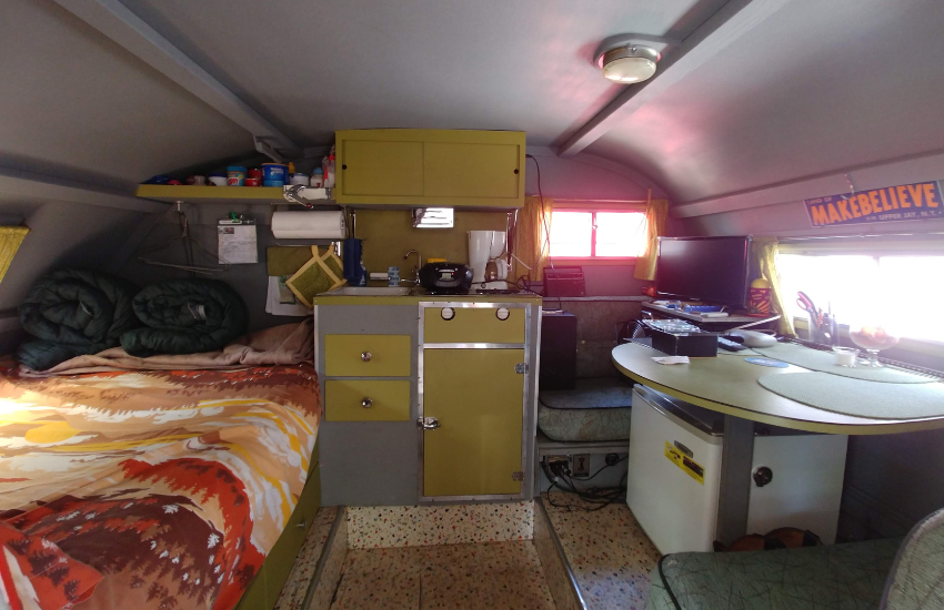 Green cabinets and bright patterned bed sheets in a retro RV camper.