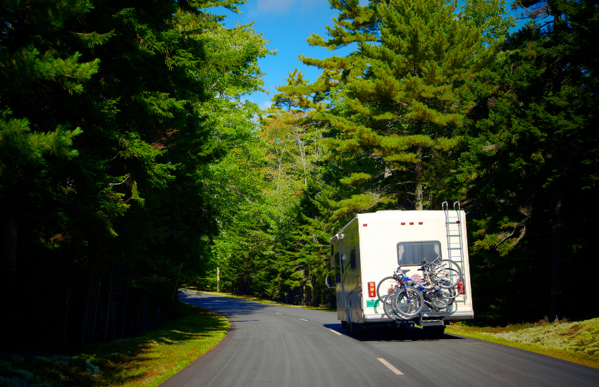 An RV camper driving along a forested road.