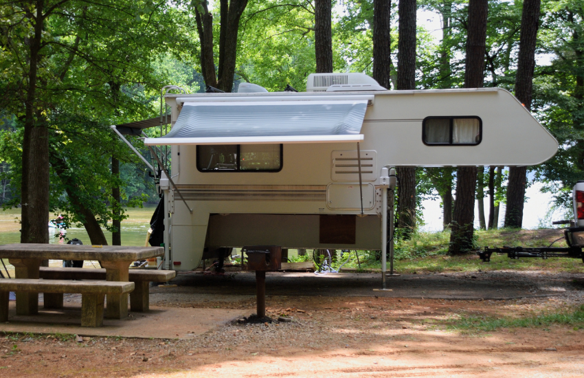 Truck Bed RV Camper A truck camper dismounted in a campground next to a picnic table.
