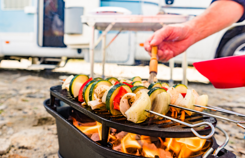 A vegetable skewer on a grill near a camper.