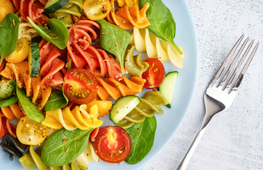 A pasta salad on a plate with a fork next to it.