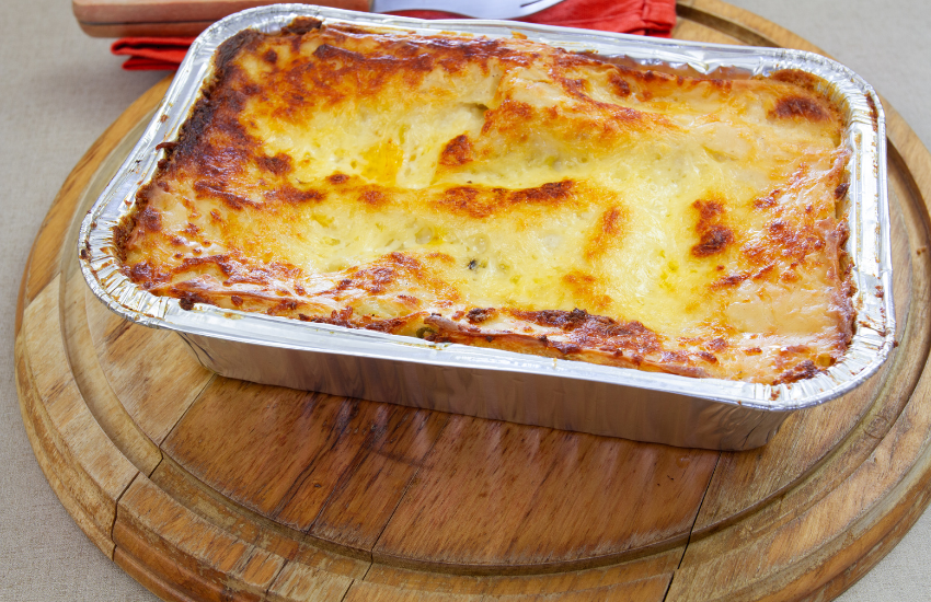 Lasagna in a foil tray on a wooden board.