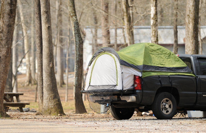 A truck tent in the back of a pickup at a campground.