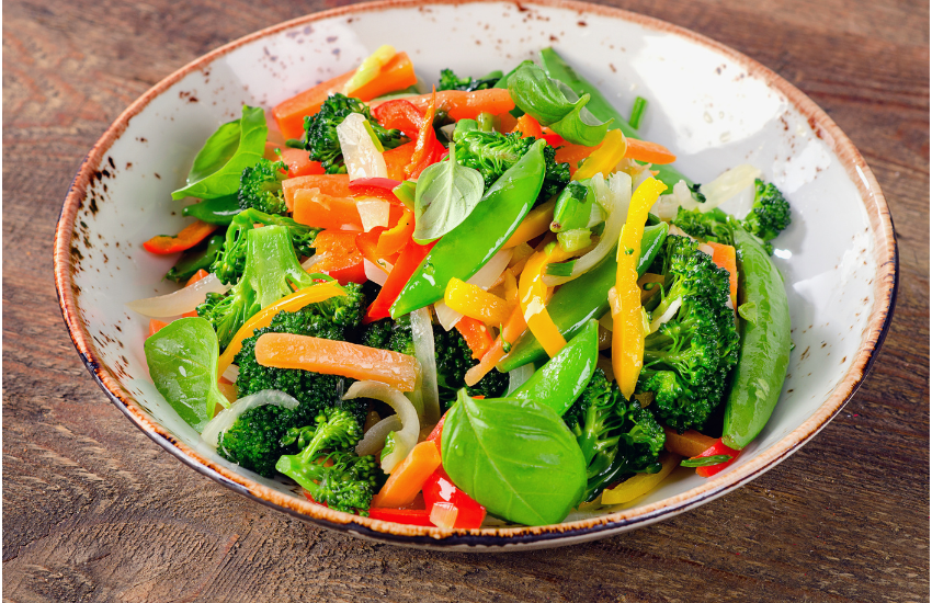 A bowl of vegetable stir fry on a wooden surface.